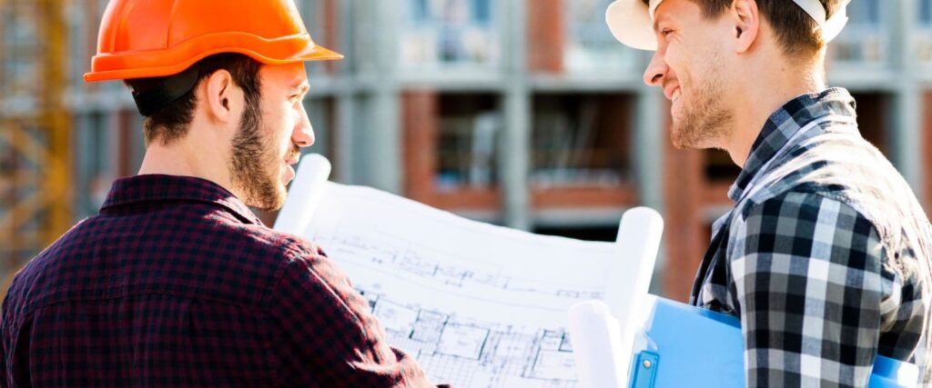 A construction professional and a homeowner are reviewing architectural blueprints on their work site. 