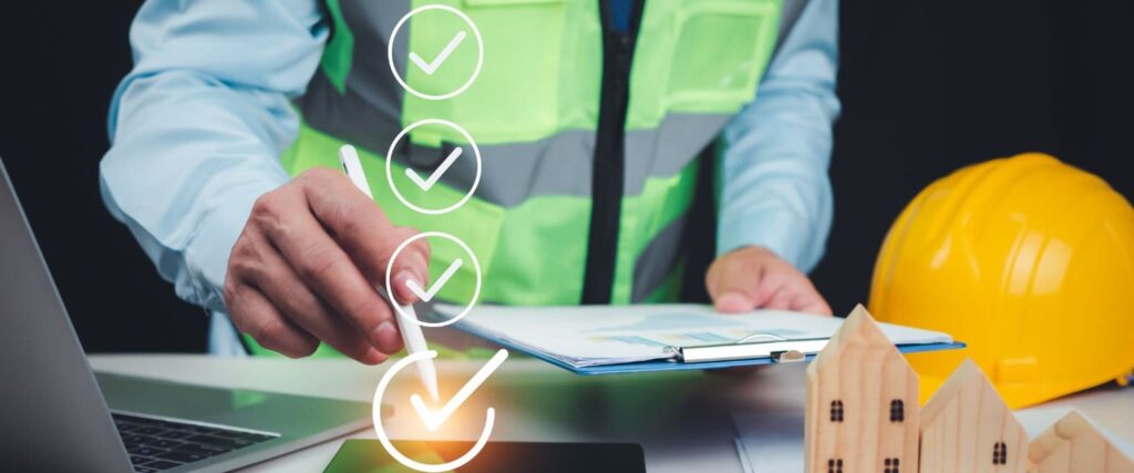 A construction project manager in a safety vest reviews documents and a digital checklist on a tablet to ensure compliance and project safety