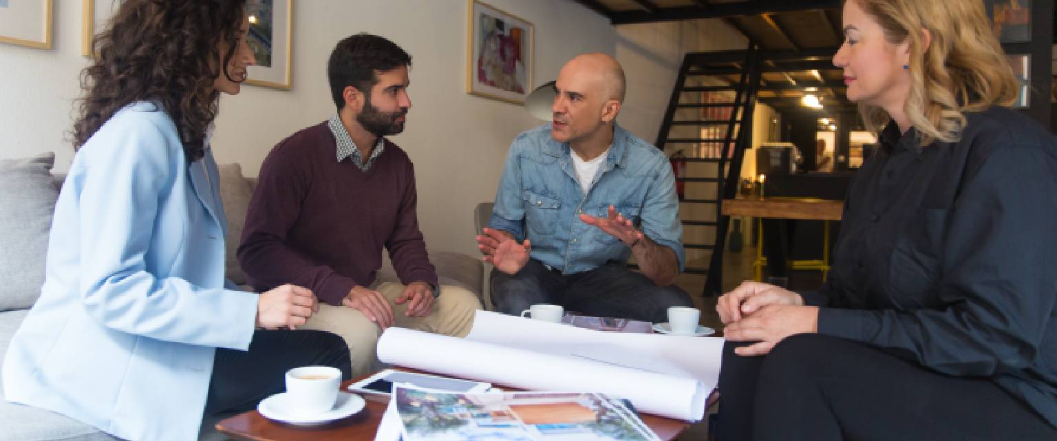 Homeowners meeting with a builder to plan a home renovation, reviewing blueprints, design samples and ideas together