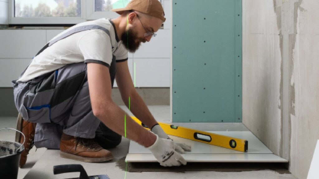 Home builder installing floor tiles during a bathroom renovation using a spirit level.